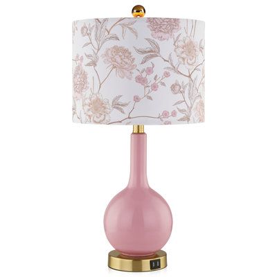 a pink table lamp with a gold base and floral fabric shade on the top, sitting on a white background