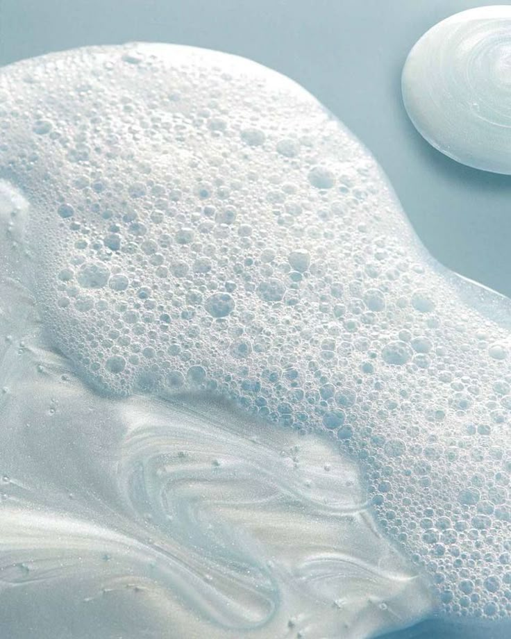 a close up of soap bubbles on a blue surface next to a white plate with an object in the background