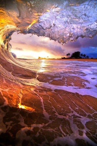 an ocean wave with the sun setting in the background and water crashing over it's surface