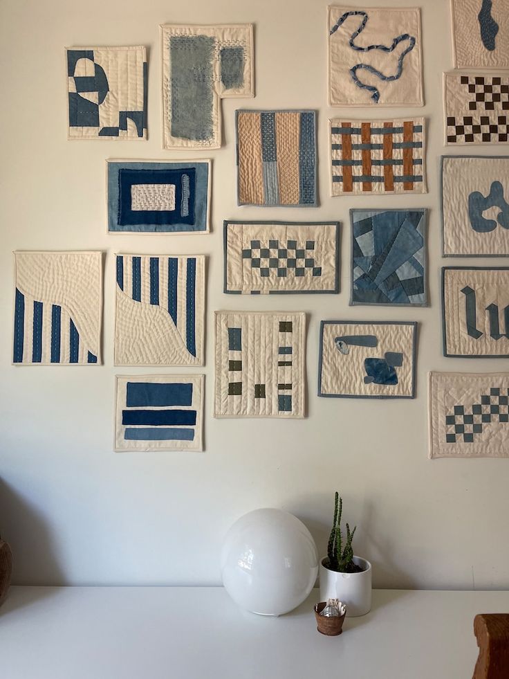 a white vase sitting on top of a table next to a wall covered in quilts