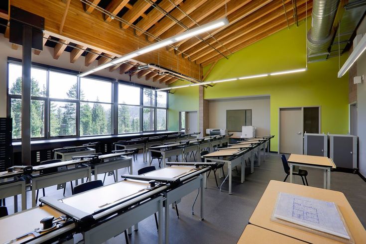 an empty classroom with desks and chairs in front of large windows overlooking the woods