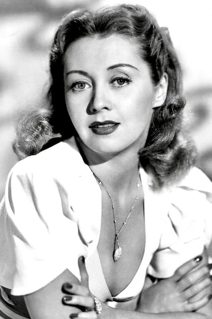 an old black and white photo of a woman with her hands on her chest, posing for the camera