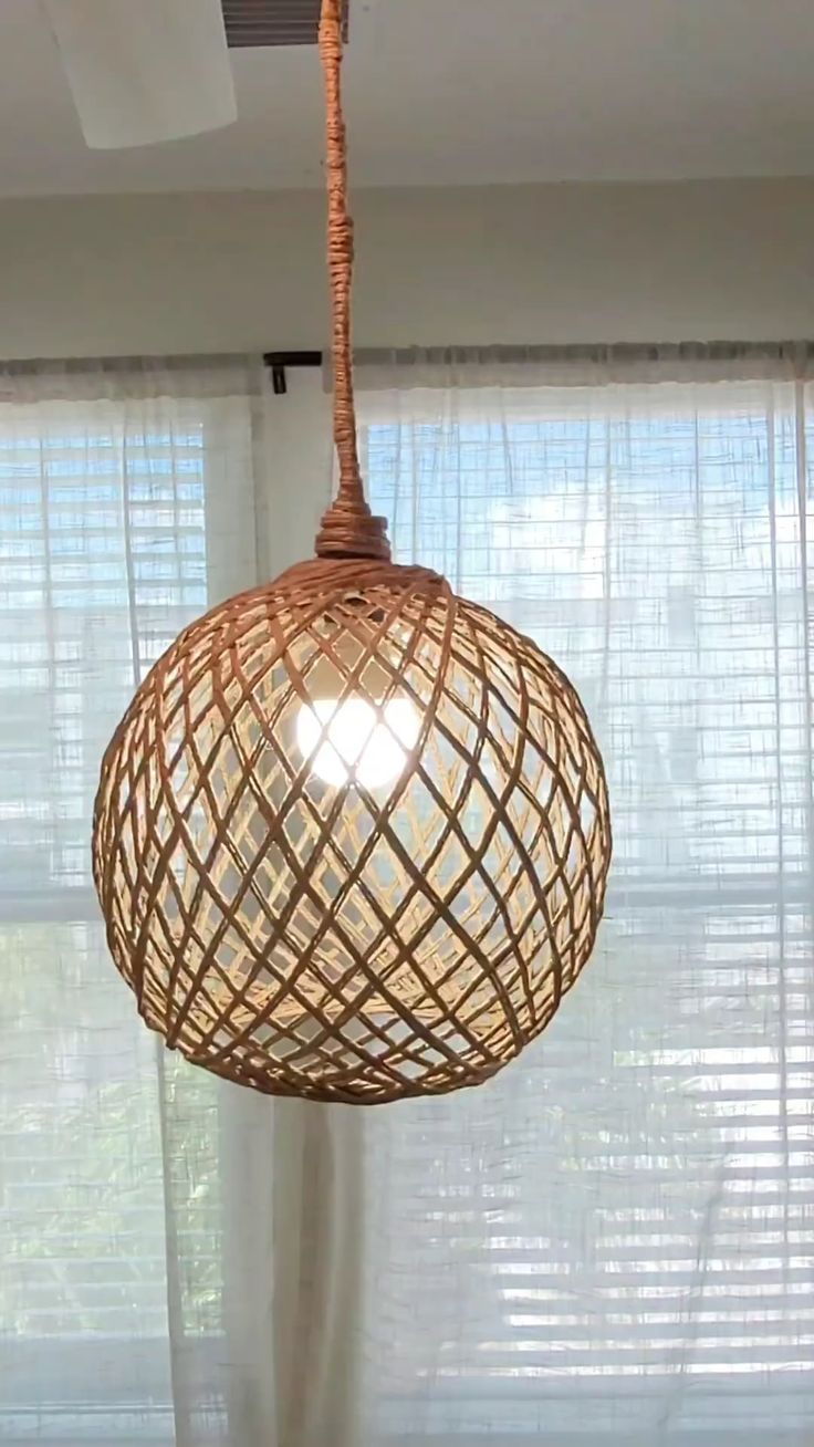 a light fixture hanging from the ceiling in front of a window with sheer drapes