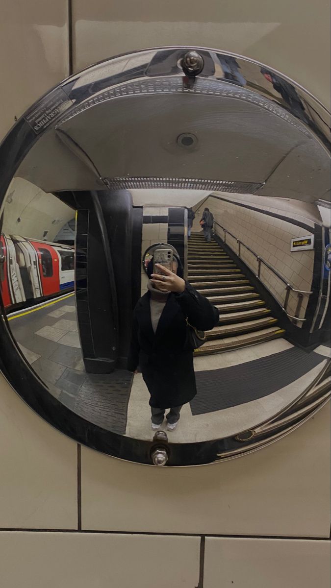 a woman taking a selfie in front of a mirror on the wall next to an escalator