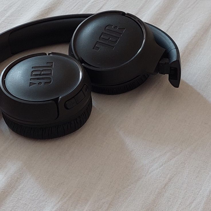 two black headphones sitting on top of a bed