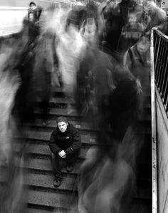 black and white photograph of man sitting on train tracks with other people in the background