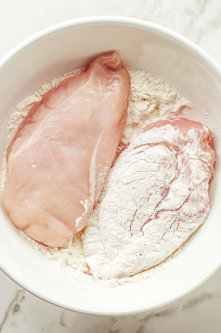 two pieces of meat in a bowl on a marble counter top with flour and other ingredients