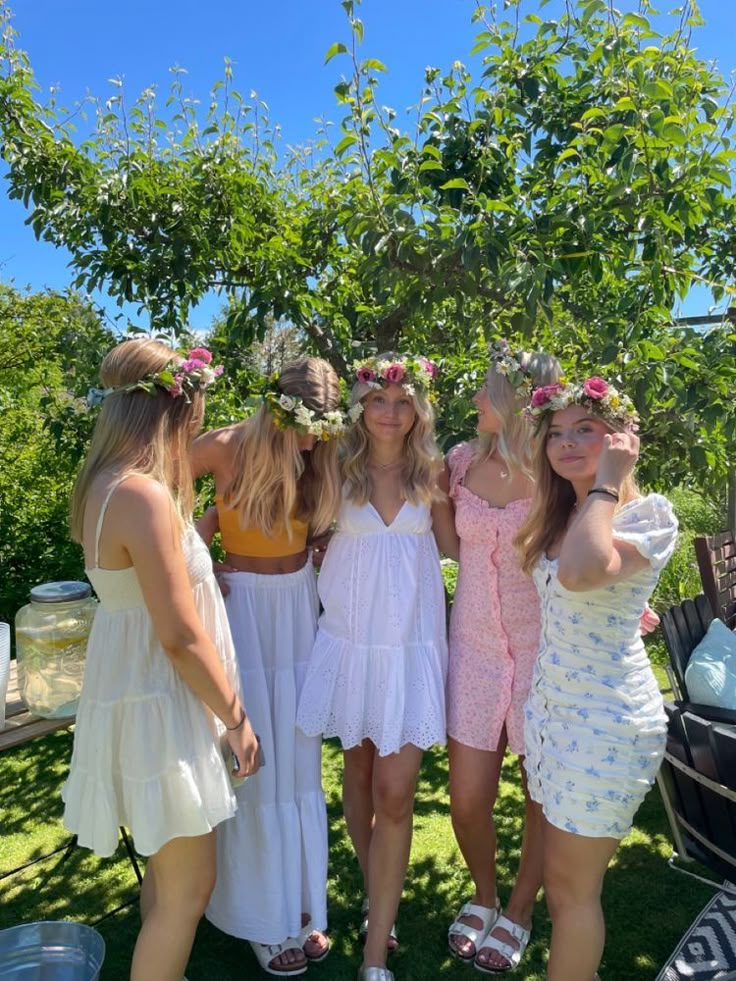 four women in dresses are posing for the camera with their arms around each other while wearing flower crowns