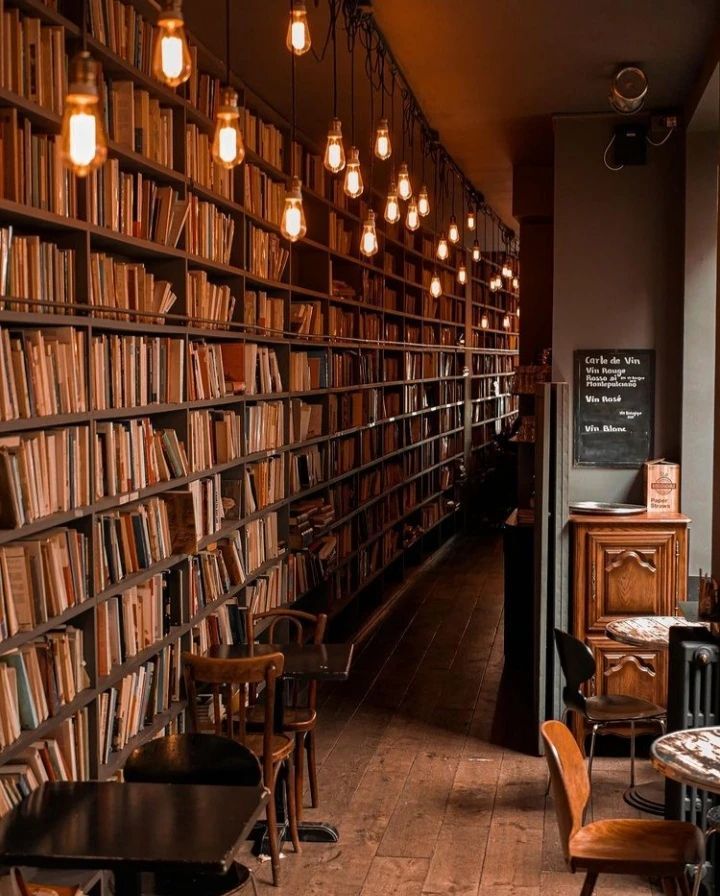 a long row of bookshelves filled with lots of books next to tables and chairs