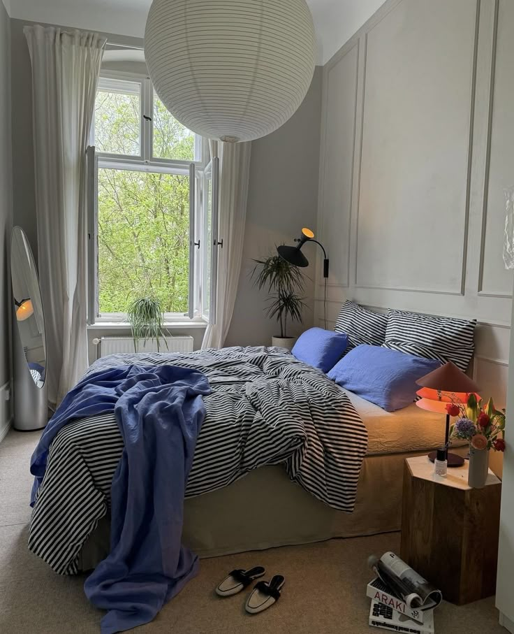 a bed room with a neatly made bed next to a window and a plant on the floor