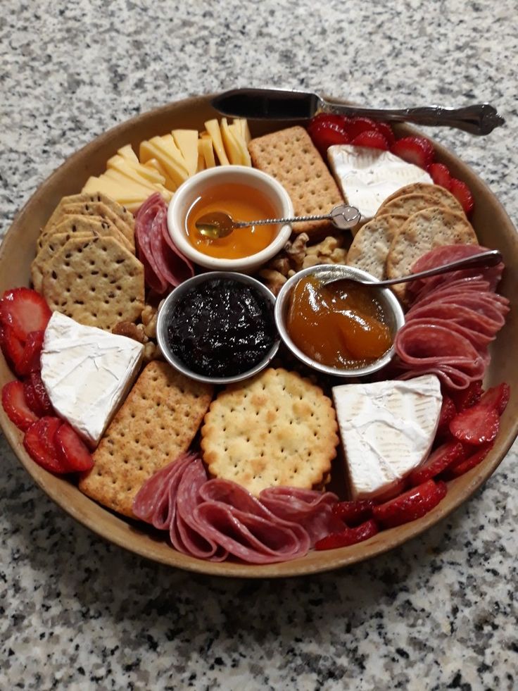 a platter filled with cheese, crackers, strawberries and jam on a table