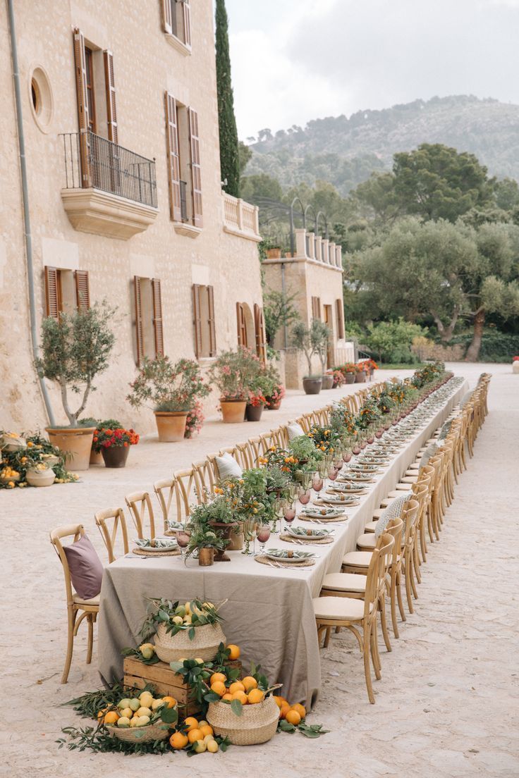 a long table is set up outside in front of a building with potted plants