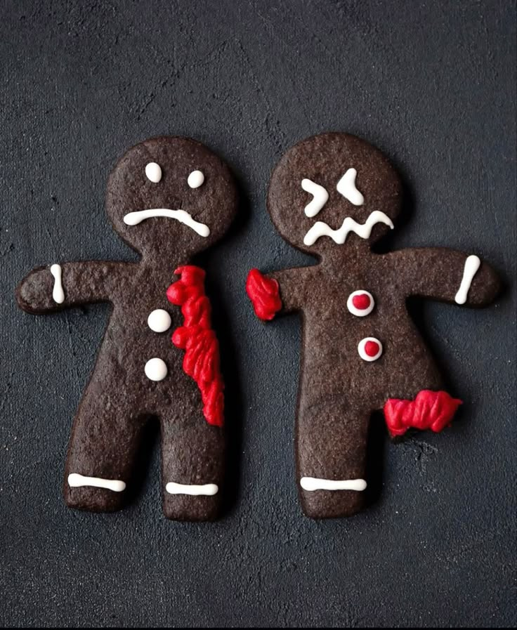 two decorated gingerbreads on a black surface with white and red icing around them