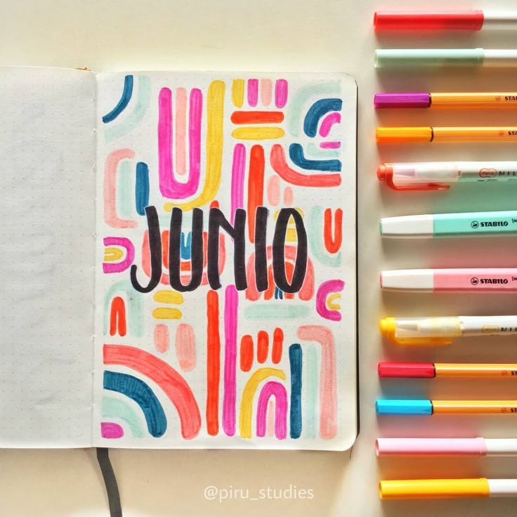 an open notebook sitting on top of a table next to markers and pens with the word june written in it