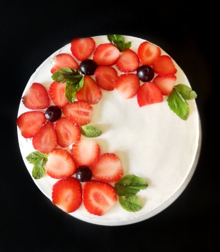 a cake decorated with strawberries and mint leaves on a black tablecloth, ready to be eaten