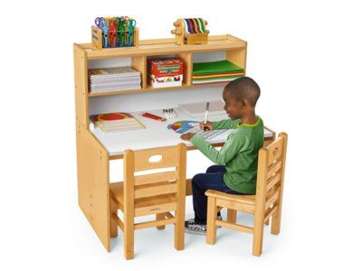 a young boy sitting at a desk with a book and pencils in his hands