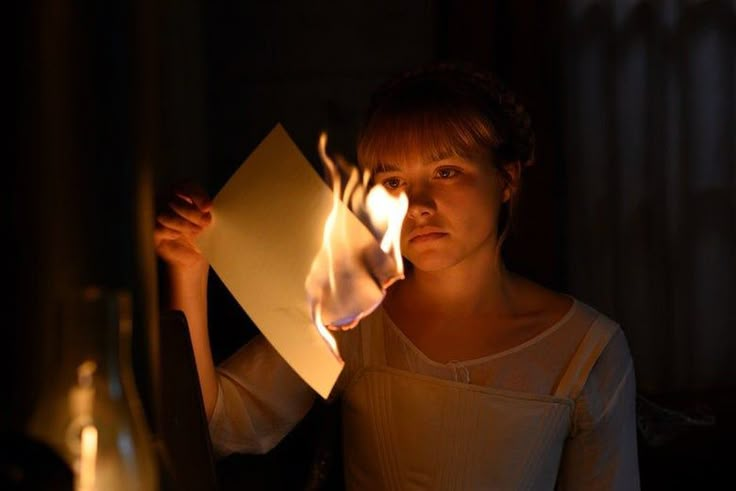 a woman holding up a piece of paper with flames coming out of it in front of her