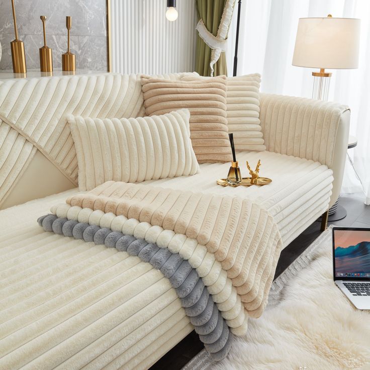 a laptop computer sitting on top of a white couch next to pillows and rugs