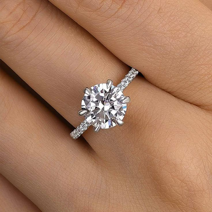 a woman's hand with a diamond engagement ring on her left hand and the center stone is surrounded by pave diamonds