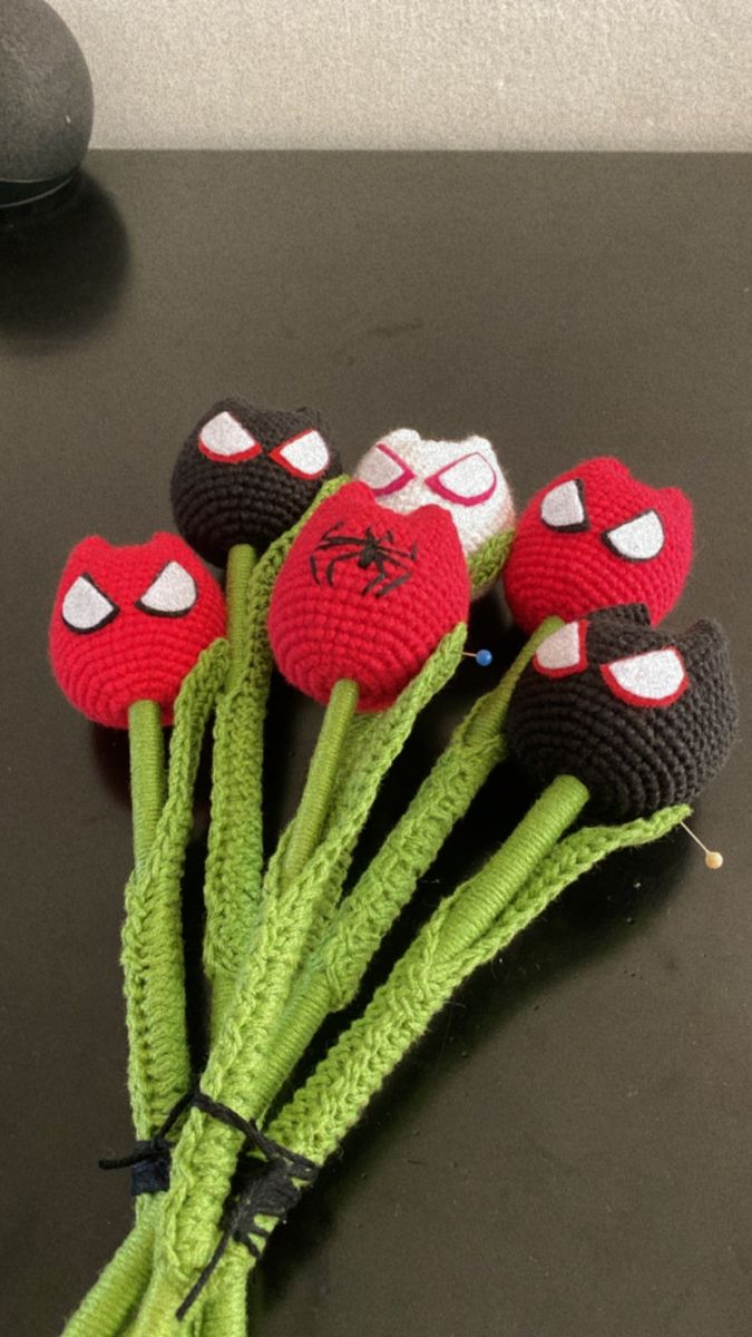 four crocheted red and black flowers sitting on top of a table next to a computer mouse