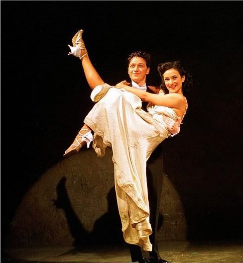 a man and woman dancing on stage in white outfits with one leg up, the other holding her