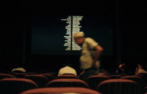 a man standing in front of a projection screen on top of a theater floor with red chairs