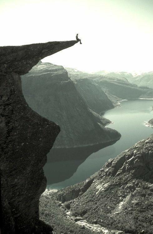 a man standing on top of a cliff next to a lake in the middle of nowhere