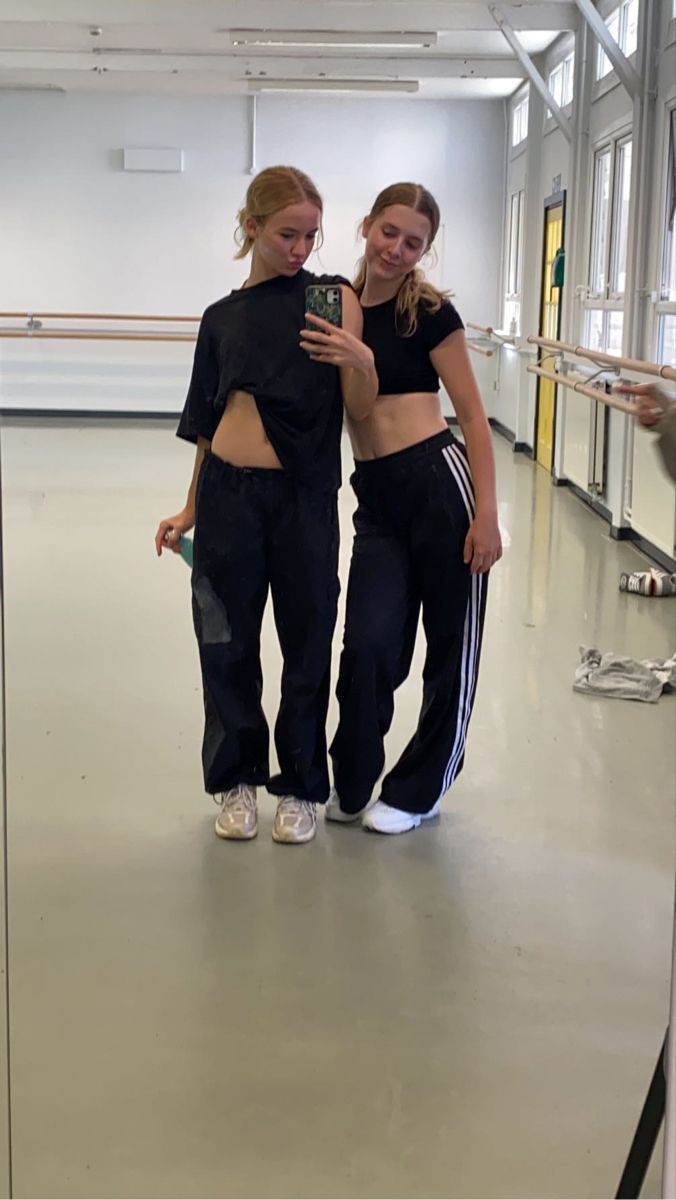 two young women standing next to each other in a dance studio looking at a cell phone