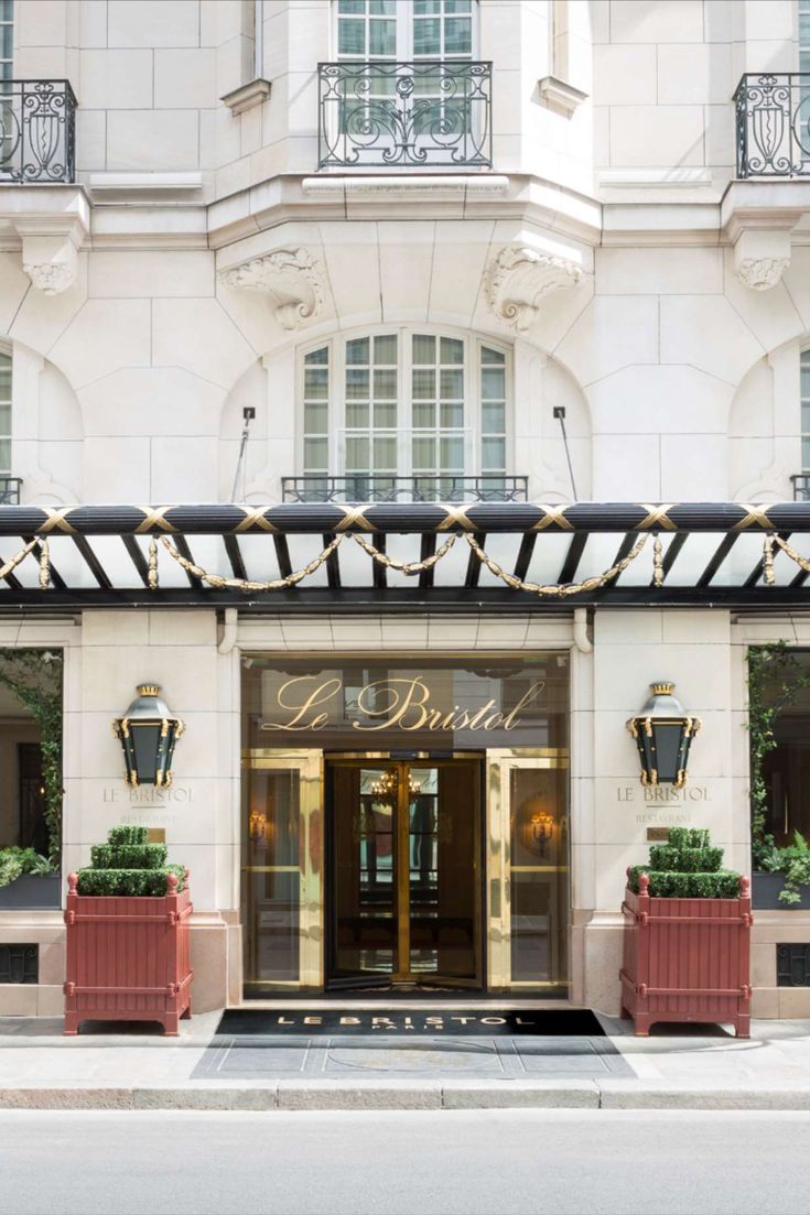 the entrance to a hotel with two red planters in front of it and an awning