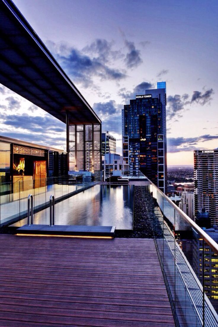 an outdoor swimming pool in the middle of a city at dusk with skyscrapers behind it