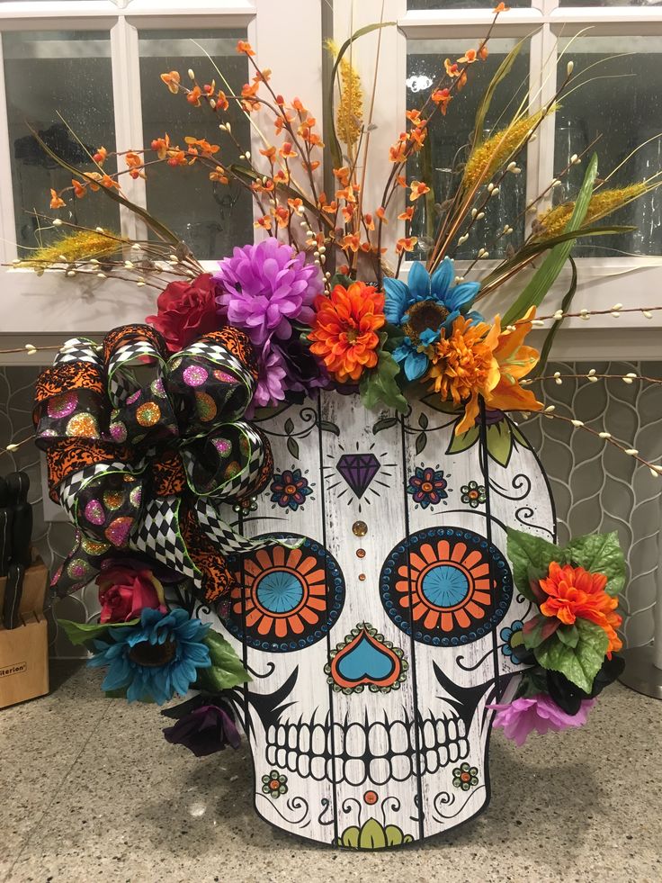 a decorated sugar skull with colorful flowers on the top and bottom, in front of a window