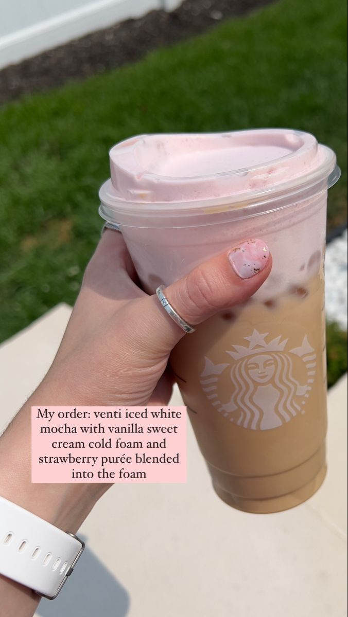 a woman's hand holding up a starbucks cup with pink frosting on it