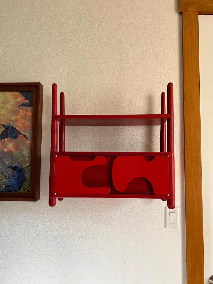 there is a red shelf on the wall next to a painting and a framed picture