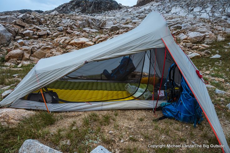 a tent pitched up on the side of a mountain with rocks and grass around it