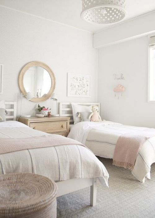 two twin beds in a white bedroom with pink and gray decor on the walls, along with a round mirror above them