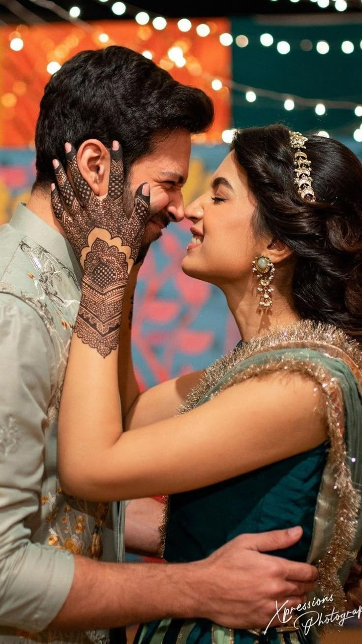 a man and woman with henna on their face kissing each other in front of lights