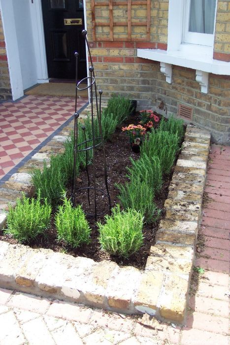 a brick house with green plants in the front yard