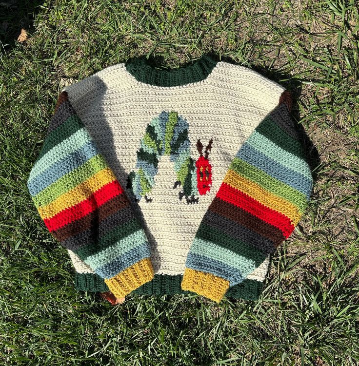 a knitted sweater sitting on top of grass in the middle of the day with an image of a caterpillar