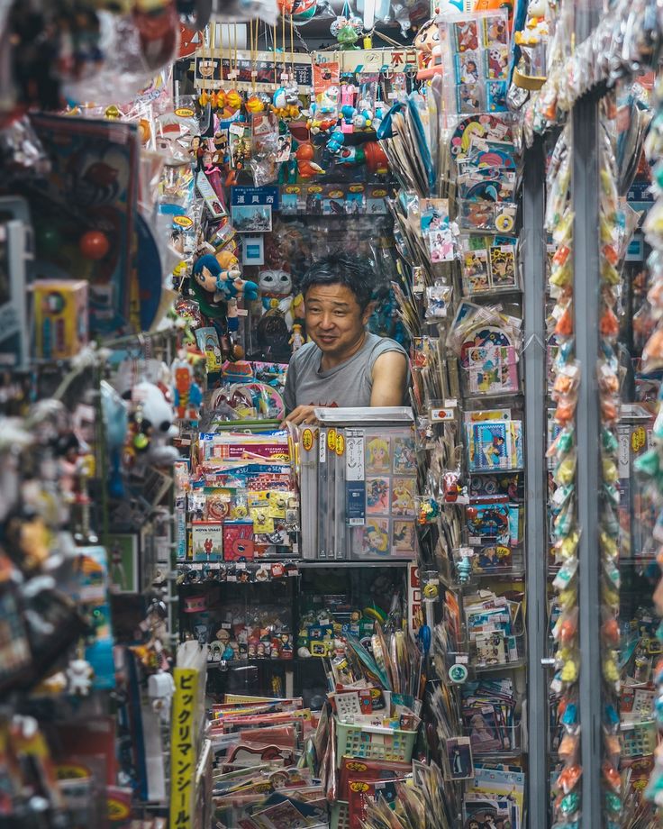 a man is sitting in the middle of a store filled with toys and other items