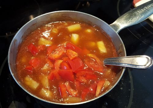 a pot filled with stew sitting on top of a stove next to a spoon and spatula