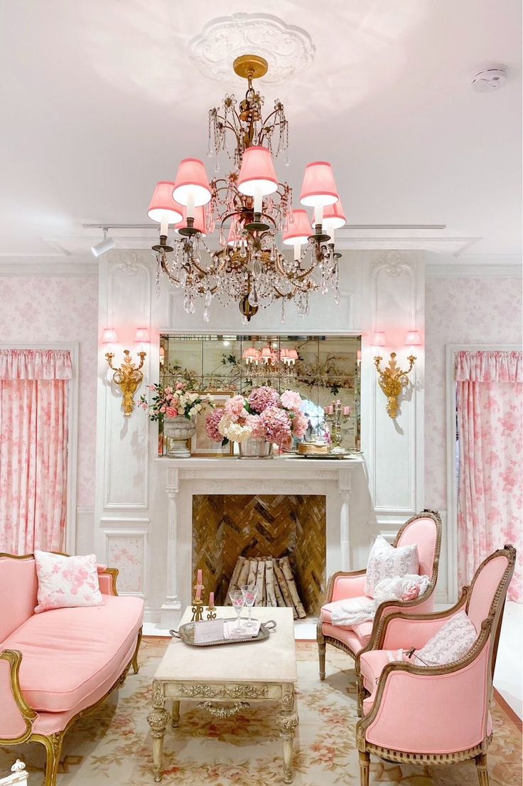 a living room with pink furniture and chandelier above the fire place in front of a fireplace