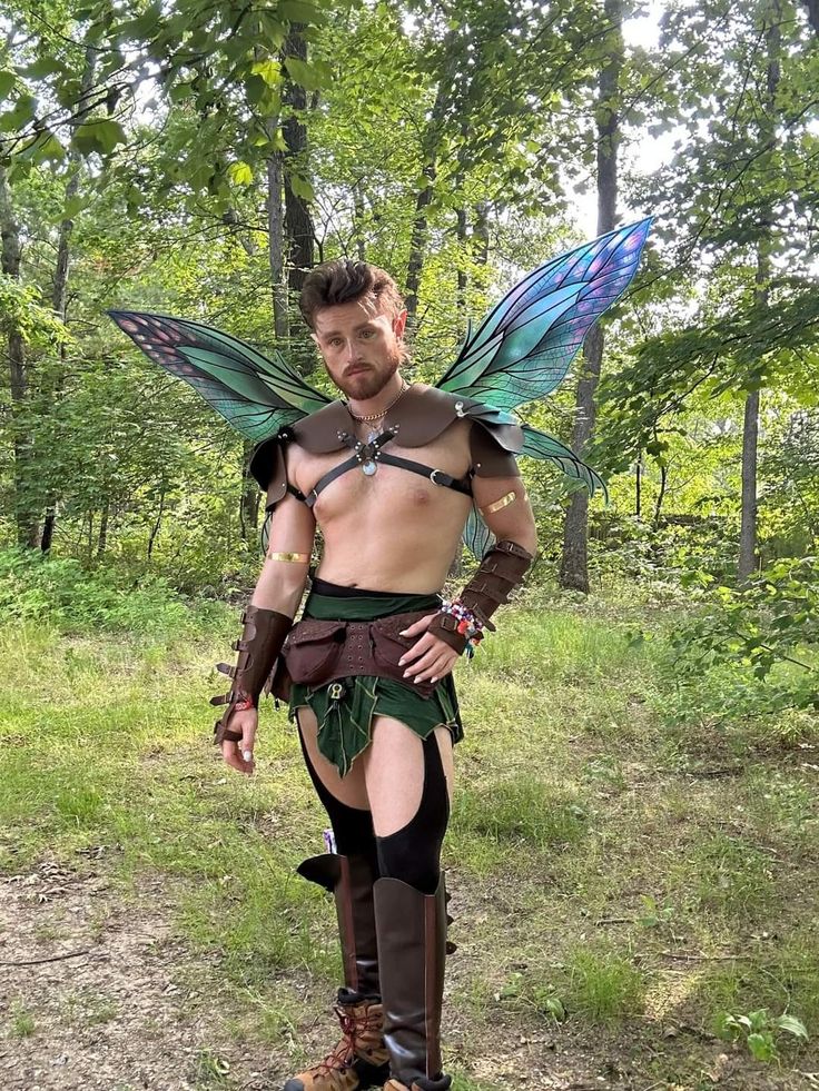 a man dressed up as tinkerbell standing in the woods with his hands on his hips