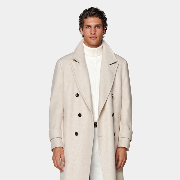 Mid-thigh length overcoat in sand, featuring wide peak lapels and natural shoulders. Double-breasted closure, patch pockets, and inside pockets for functionality. Single vent, lined, with martingale belt for style. Luxury Cream Outerwear With Double Button Closure, Luxury Beige Double-breasted Wool Coat, Luxury Cream Double-breasted Outerwear, Luxury Beige Double-breasted Pea Coat, Neutral Long Wool Coat, Luxury Beige Wool Coat With Concealed Placket, Formal Beige Wool Coat With Concealed Placket, Beige Wool Coat With Notch Lapel And Hidden Buttons, Beige Long Wool Coat With Concealed Placket