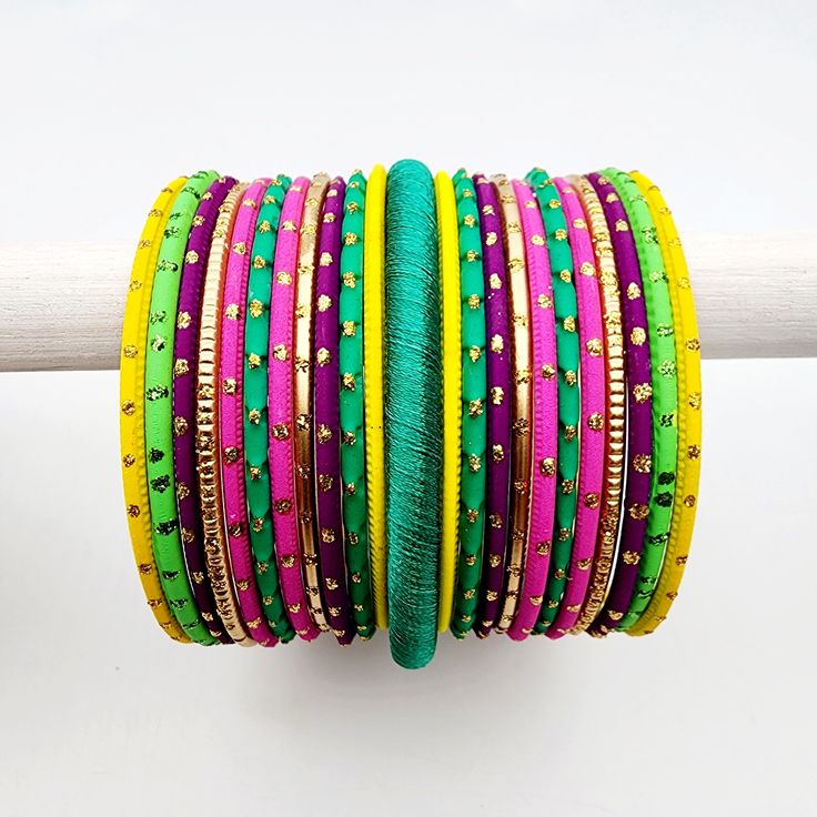 Get ready to shine with the Nyati Banglez Box, a vibrant collection of neon-inspired bangles perfect for the festive season! This box includes a dazzling mix of silk thread bangles, along with matte, shiny, and glitter finishes, all designed to help you create bold and beautiful sets. Framed by four elegant gold-plated metal ball bangles, the Nyati Box features bright hues like hot pink, yellow, emerald, purple, tangerine, and more. Plus, it comes with a matching bindi to complete your look! Mix and match to make endless unique combinations—examples shown in pictures for inspiration. *free matching bindi included *please note bangle boxes are final sale. *colour tones may appear slightly different in person than on screen. Purple Bracelets For Festivals And Gifts, Adjustable Purple Bangle For Festive Occasions, Festive Multicolor Bangle, Handmade Green Bollywood Bracelets, Handmade Green Bangle For Party, Adjustable Yellow Bangle For Festive Occasions, Festive Adjustable Yellow Bangle, Adjustable Multicolor Bangle For Diwali, Multicolor Bangle For Diwali Festival