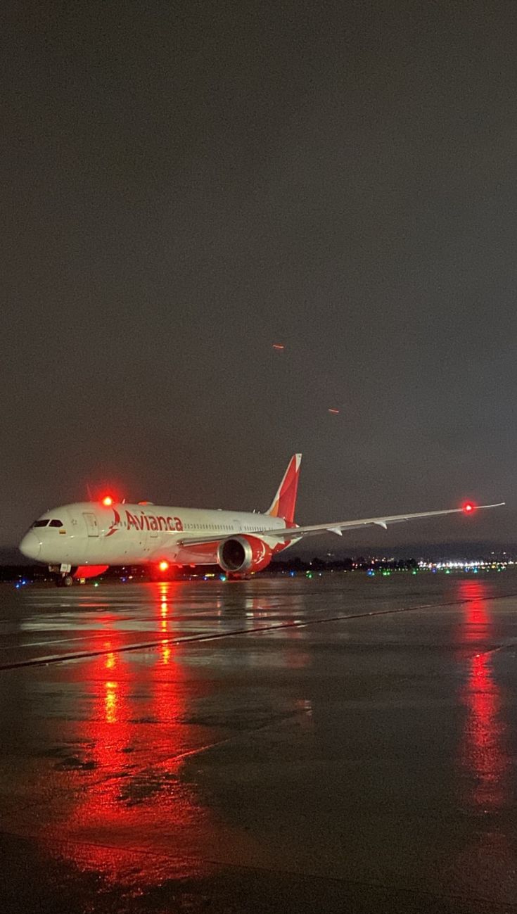 an airplane sitting on the runway at night with lights reflecting off it's wing