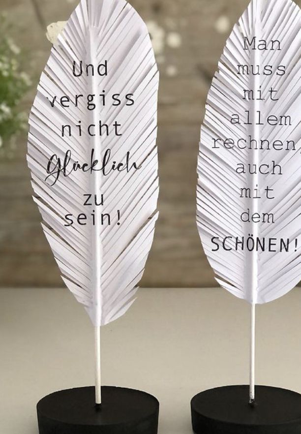 two white feathers with words on them sitting on top of a black stand in front of a wooden wall