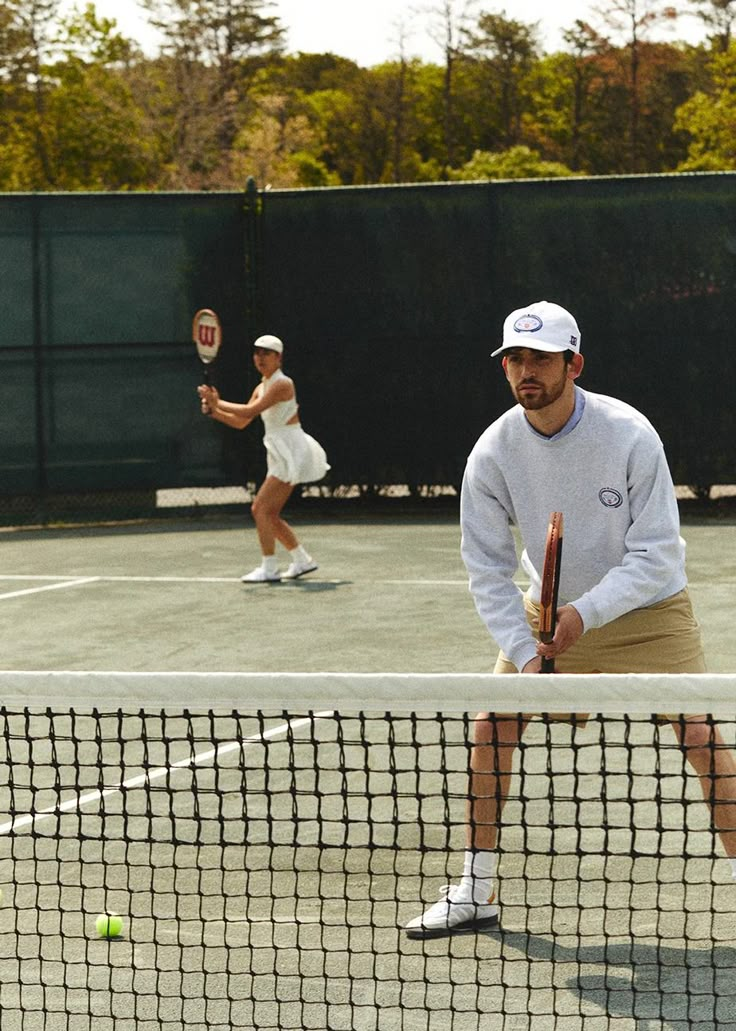 two people playing tennis on a court with trees in the background and one person holding a racket