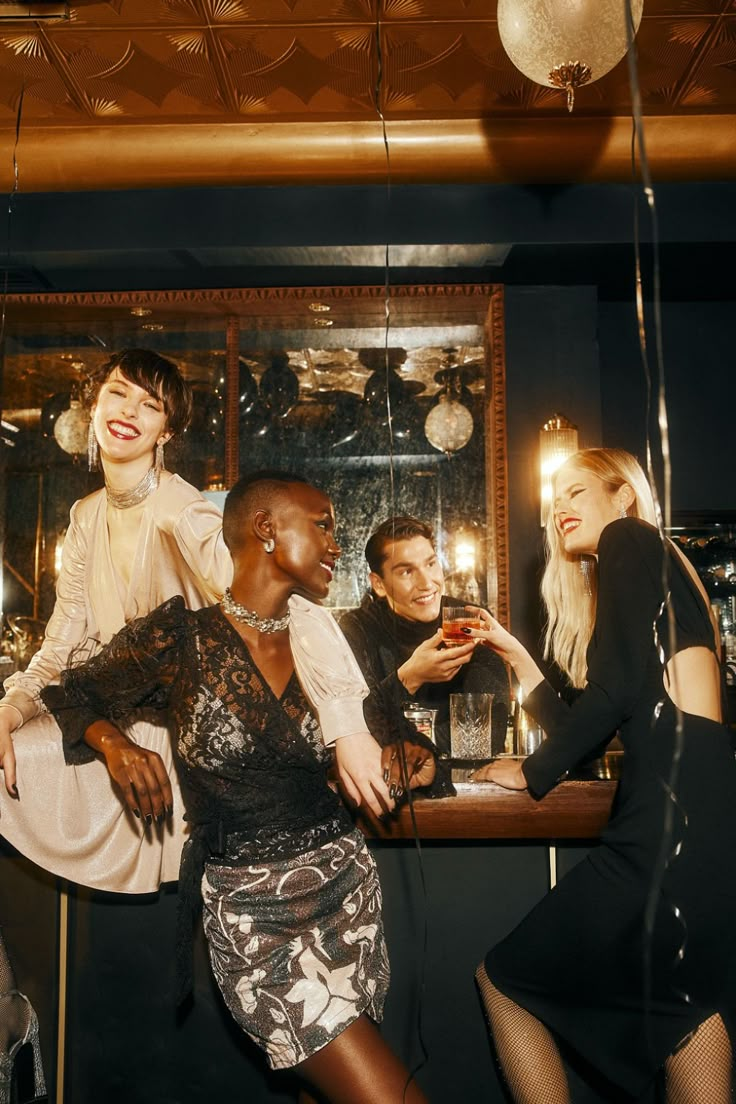 three women and one man are posing for the camera in front of a bar with candles