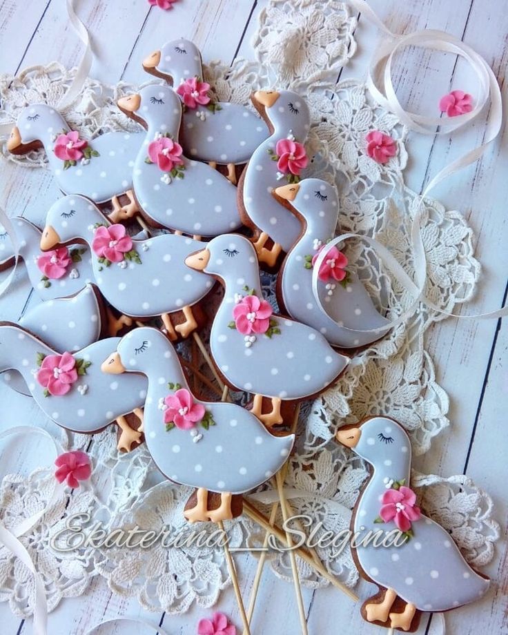 decorated cookies in the shape of ducks with pink flowers and bows are on a lace doily