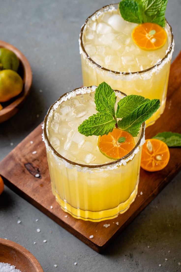 two glasses filled with orange juice and garnished with mint on a cutting board